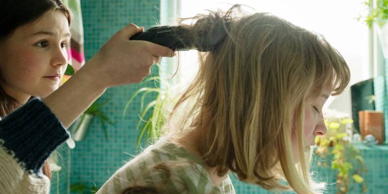 Ein Mädchen rasiert die langen Haare eines anderen Mädchen ab.